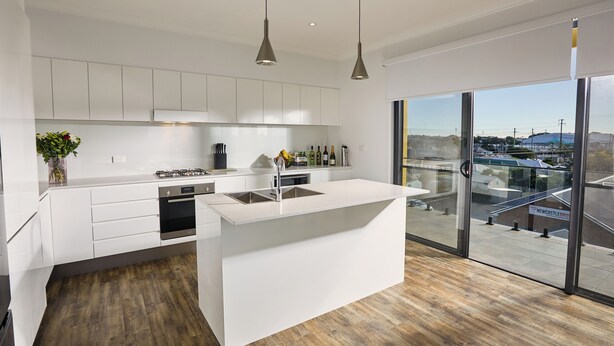 A modern kitchen with white cabinetry, a central island, and a large window offering a view of the outside. - Nouveau Serviced Apartments (Newcastle)