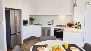A modern kitchen with white cabinets, stainless steel appliances, and a breakfast setup on the dining table. - Nouveau Serviced Apartments (Newcastle)