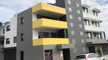 A modern multi-story building with a flat roof, a yellow accent wall, and a grey facade.