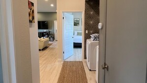Un pasillo con alfombra que conduce a un dormitorio con cama y cómoda. Se ve una puerta a la derecha y un televisor al fondo.