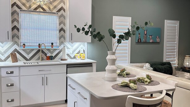 Una cocina moderna con armarios blancos, una isla central y una zona de comedor con dos sillas.