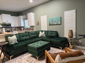 A modern living room with a sectional sofa, a dining area, and a kitchen in the background. - The Bohemian 2BR Near Hospital, Bay & Cole Park (Corpus Christi)