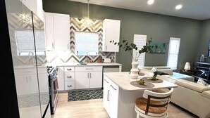 Una cocina moderna con armarios blancos, una isla central y un comedor con una silla.