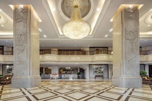 Un vestíbulo espacioso con techo alto, columnas ornamentadas y una lámpara central.