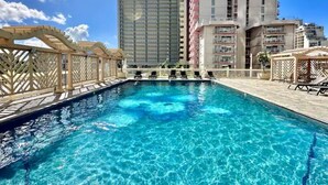 Une piscine à l’eau d’un bleu cristallin, entourée d’une terrasse en bois et de chaises longues.