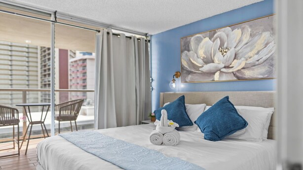 Une chambre d’hôtel avec un lit, un grand tableau représentant des fleurs et un balcon avec des chaises.