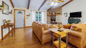 A living room with a sofa set, a wooden coffee table, a ceiling fan, and a stone fireplace.