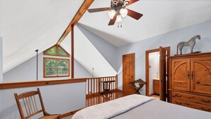 A bedroom with a sloped ceiling, a wooden rocking chair, a bed with a quilt, a wardrobe, and a small table.