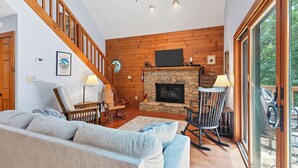 A spacious living room with a stone fireplace, wooden ceiling, and a large window.