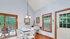A dining area with a table and chairs, a hanging light fixture, and a view through large windows.