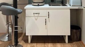 A compact kitchenette with a microwave, stove, sink, and a small bar stool.