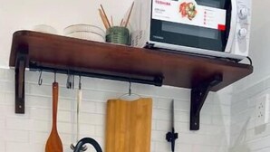 Una cocina con encimera blanca, un mueble verde oscuro, una tabla de cortar de madera, un microondas y un colgador para utensilios.