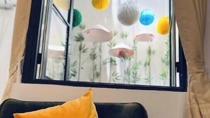 Una habitación con ventana, un sofá oscuro con un cojín amarillo y vistas a decoraciones de papel de colores en el exterior.