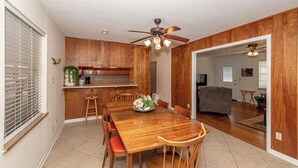 A dining area with a wooden table and chairs, a kitchen with wooden cabinets, and a ceiling fan.