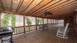 A covered wooden deck with a grill, chairs, and a ceiling fan.