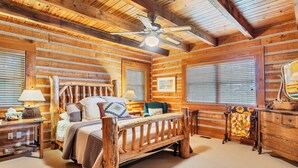 A log cabin bedroom with a wooden bed, two bedside tables, a nightstand, a dresser, a ceiling fan, and large windows with blinds. - TRANQUILITY 4 BR 4 1/2 Bath Log Cabin with Acreage and Views for Miles (Townsend)