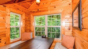 A wooden cabin room with a large table, two windows, and a bench. - Authentic log cabin with the real feel of serenity in a Golf Course Vicinity. (Townsend)