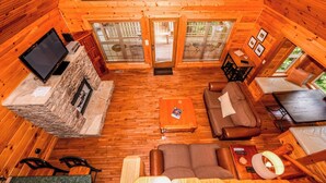 A cozy cabin interior with a stone fireplace, wooden flooring, a sofa, a coffee table, and a television. - Authentic log cabin with the real feel of serenity in a Golf Course Vicinity. (Townsend)