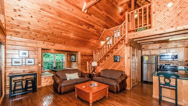 A log cabin interior with a wooden staircase, a living room with a sofa and coffee table, and a kitchen area. - Authentic log cabin with the real feel of serenity in a Golf Course Vicinity. (Townsend)