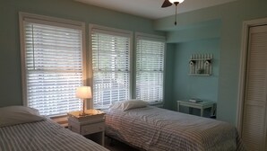 A bedroom with two beds, a nightstand with a lamp, a small table, and a ceiling fan. - This cozy home is located on a situated on a mountainside is welcoming! (Townsend)