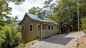 A rustic cabin with a sloped roof, a porch, and a gravel driveway surrounded by trees. - This cozy home is located on a situated on a mountainside is welcoming! (Townsend)