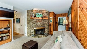 A cozy living room with a stone fireplace, a wooden wall, a sofa, and a bookshelf. - This cozy home is located on a situated on a mountainside is welcoming! (Townsend)