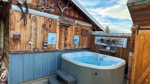 Una baita di legno con vasca idromassaggio, scalini in legno e varie decorazioni, tra cui intagli di animali e cartelli.