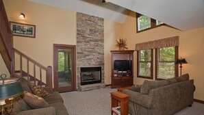 A living room with a stone fireplace, a television on a stand, a sofa, and a lamp.
