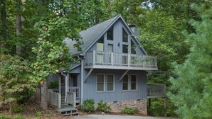 A two-story house with a stone foundation, a balcony on the upper floor, and a porch on the lower level.