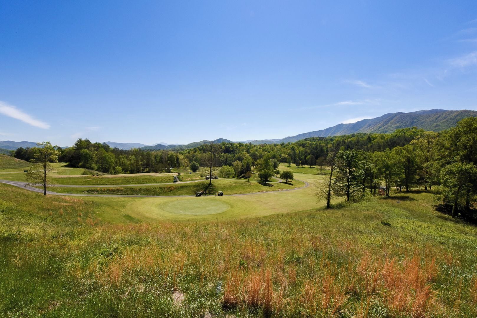 Un campo de golf con cielo despejado, colinas ondulantes y montañas a lo lejos.