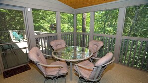 Une terrasse couverte avec une table ronde en verre et quatre chaises rembourrées.