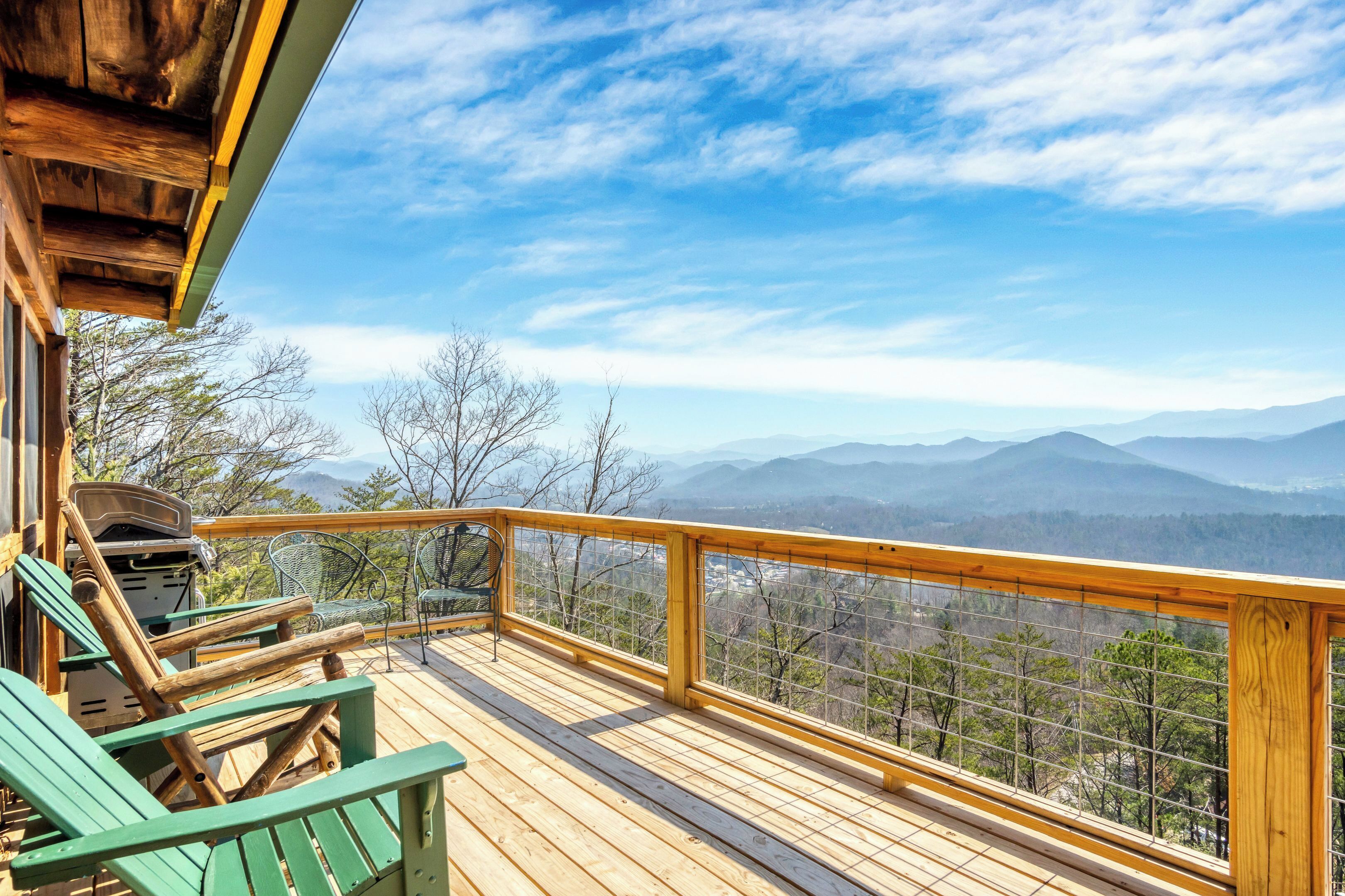 A wooden deck with a view of mountains, a grill, and green chairs.