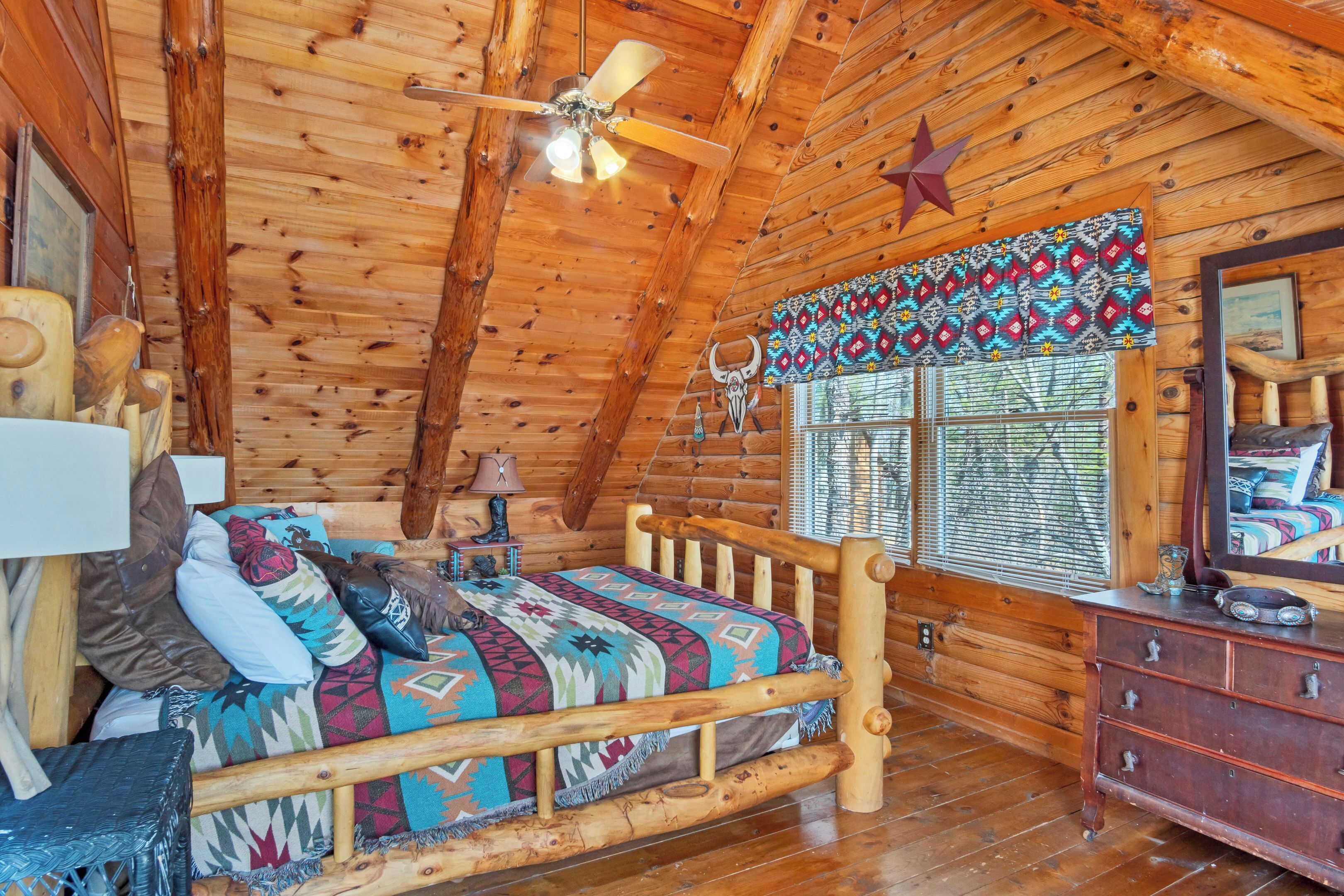 A log cabin room with a bed, wooden walls, a ceiling fan, a star decoration, and a window with patterned curtains.