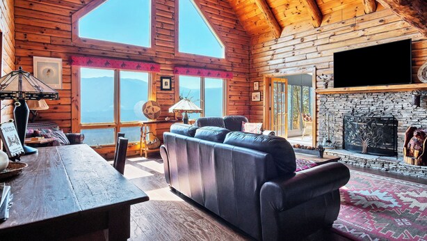 A log cabin interior with a stone fireplace, a large sofa, and a wooden dining table. - Authentic log cabin with a spectacular view !  Enjoy the seclusion and sunsets (Townsend)