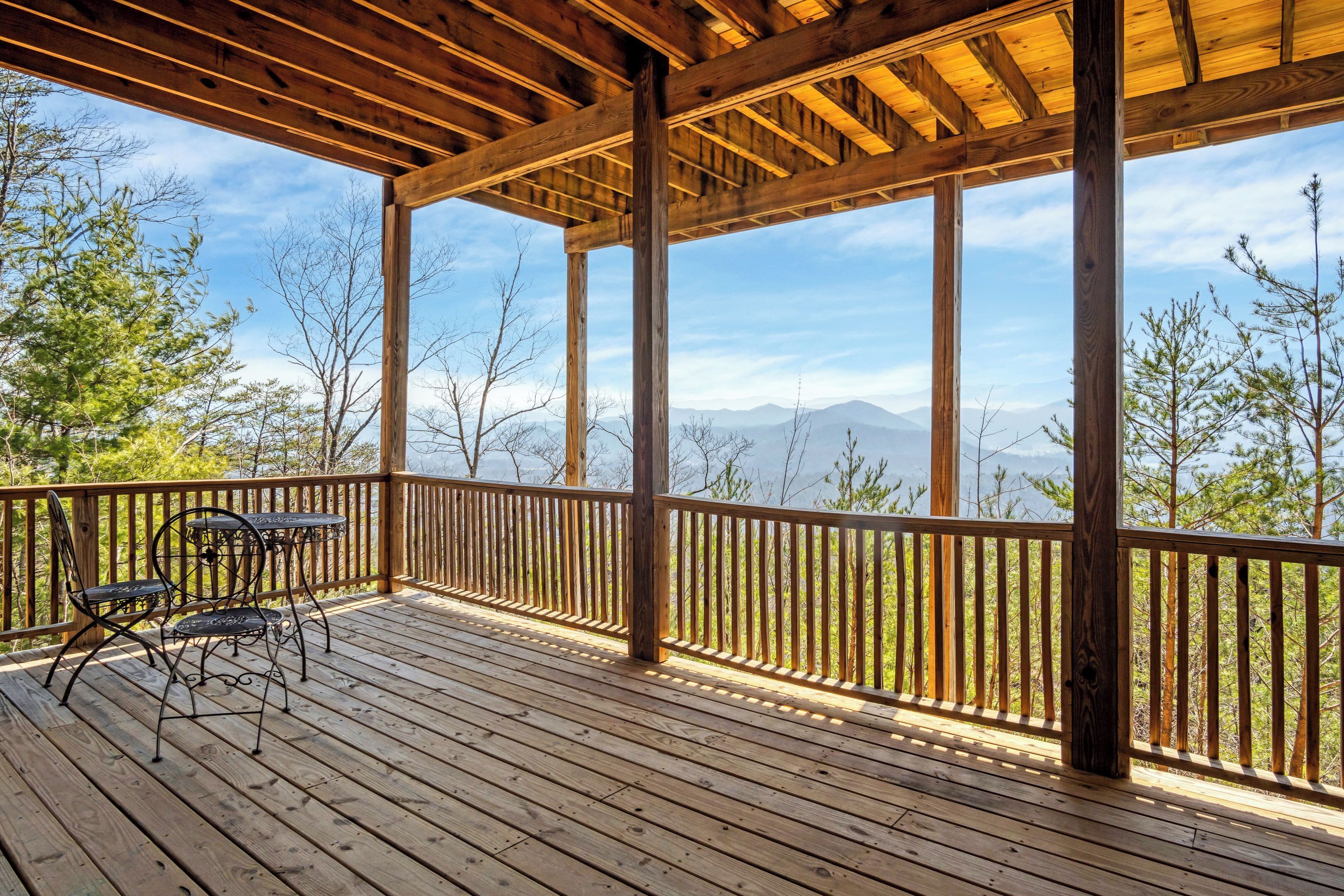 Une terrasse en bois avec une table et des chaises, offrant une vue sur un paysage montagneux.