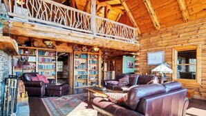 A cozy log cabin interior with a wooden balcony, leather sofas, a fireplace, and a large bookshelf. - Authentic log cabin with a spectacular view !  Enjoy the seclusion and sunsets (Townsend)