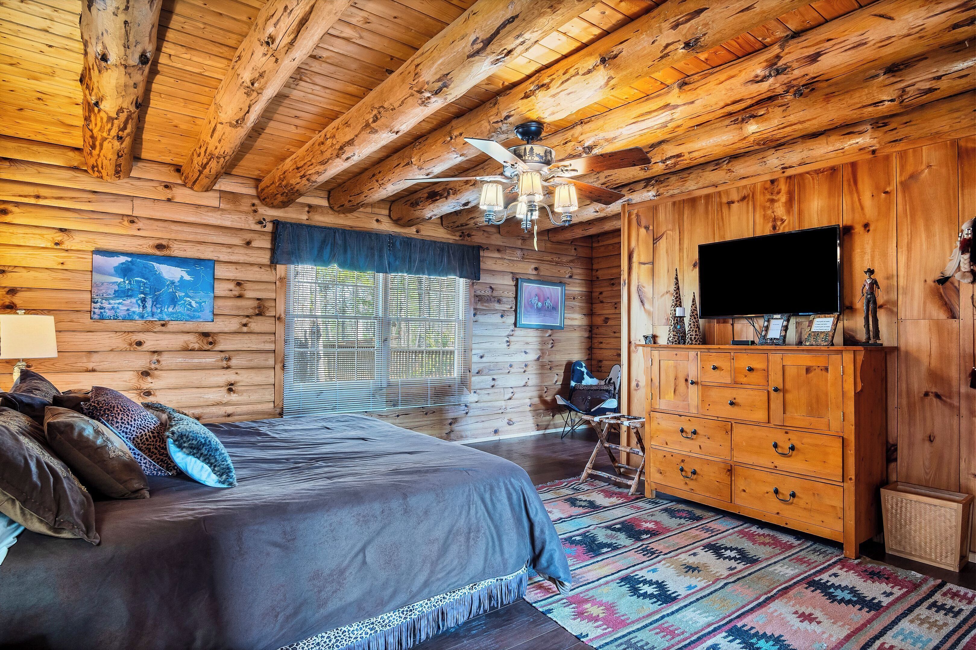 A log cabin bedroom with a large bed, wooden dresser, and a ceiling fan.