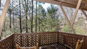 A wooden deck with lattice railings and wicker furniture, overlooking a forested area.