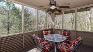 A sunroom with a round table and chairs, large windows, and a ceiling fan.