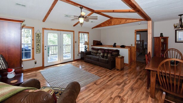 A spacious living room with wooden floors, a ceiling fan, a sofa, and a dining area with a wooden table and chairs.
