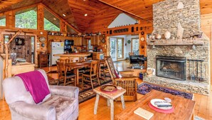 A cozy cabin interior with a stone fireplace, wooden furniture, and a kitchen area.