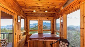 A wooden cabin with a large windowed room, a wooden bench, and a view of mountains.
