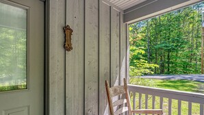 En veranda med en trästol, en vit dörr och utsikt över ett skogsområde.