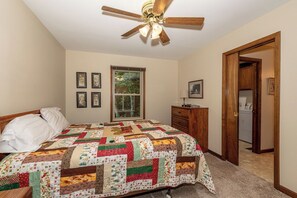 A bedroom with a large bed, a ceiling fan, a dresser, a window, and a door leading to a laundry area. - This home is located on a beautiful golf course community and has a view (Townsend)