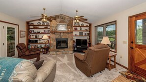 A living room with a fireplace, bookshelves, a television, and a ceiling fan. - This home is located on a beautiful golf course community and has a view (Townsend)