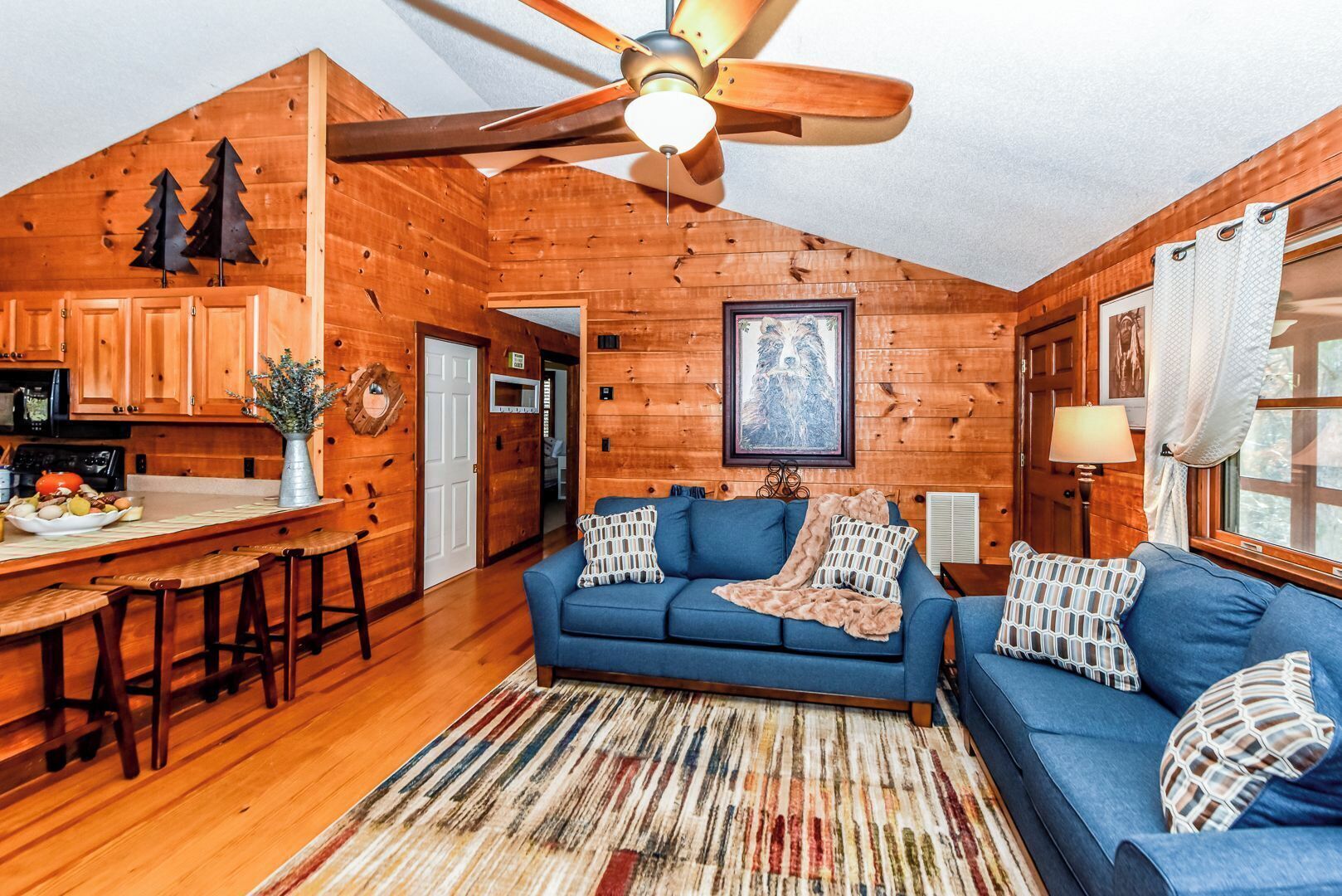 A cozy cabin interior with a wooden interior, a blue sofa, a dining area, and a ceiling fan.