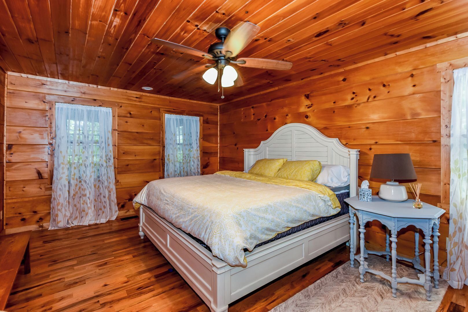 Ein Schlafzimmer einer Holzhütte mit einem Bett, einem Nachttisch, einer Lampe und einem Deckenventilator.