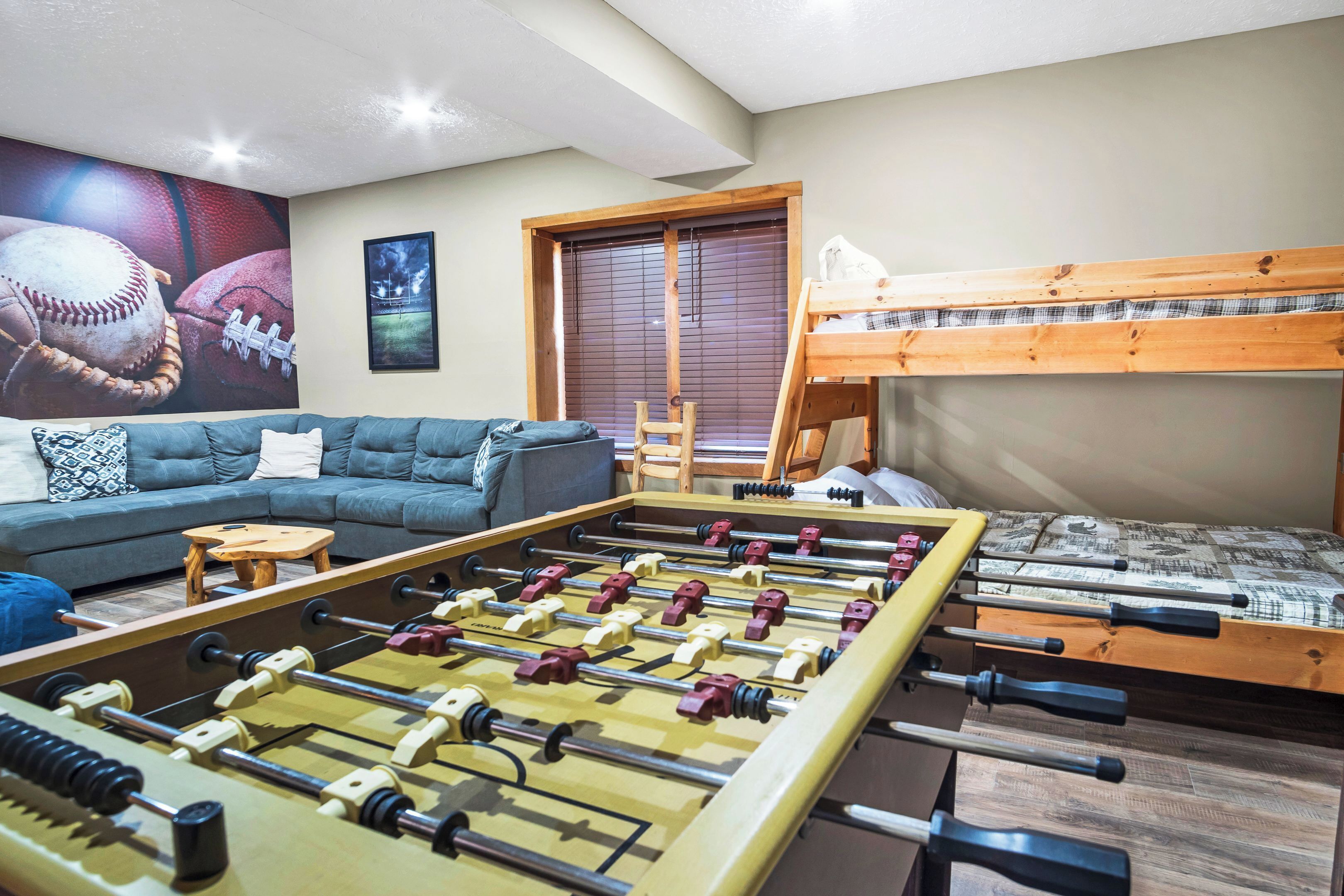 Una habitación con mesa de fútbol, sofá, literas y ventana con persianas.