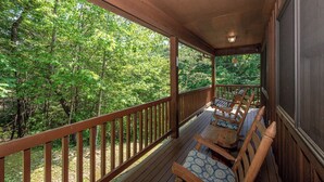 Une terrasse en bois avec une balustrade, deux chaises en bois dotées de coussins à motifs, et une vue sur une forêt dense et verdoyante.