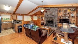 Un intérieur de chalet chaleureux avec une cheminée en pierre, des meubles en bois et un coin cuisine.